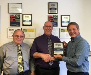 Three men in an office holding the Lubenow Transportation Platinum Award for Safety